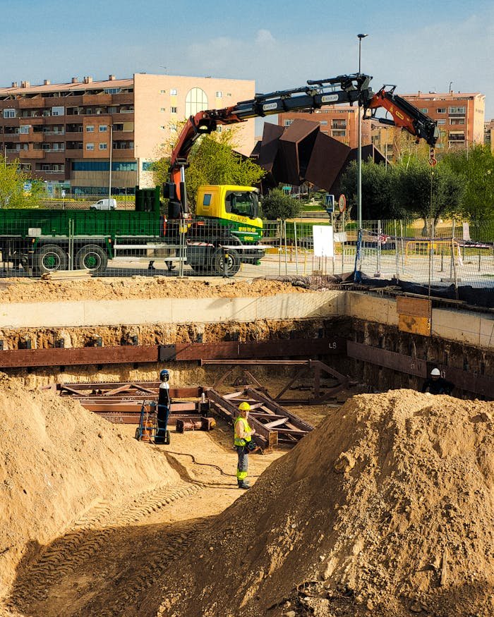 Construction workers operating at an urban site in Madrid, with machinery and residential buildings in view.